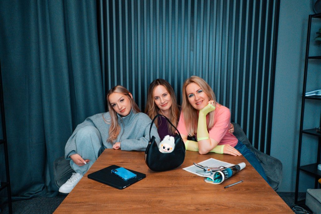 Aleksandra Marciniak, Ania Dorot i Oliwia Cech razem przy stole, symbolizując współpracę pokoleń w biznesie i marketingu
