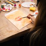 Uczestniczka warsztatów malarskich malująca usta na płótnie podczas wydarzenia „Jak malujemy swój wizerunek?” organizowanego przez Twój StartUp.