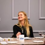 Uśmiechnięta uczestniczka warsztatów siedząca przy stole z kubkiem Twój StartUp podczas wydarzenia „Jak malujemy swój wizerunek?”.