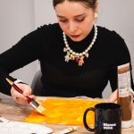 Uczestniczka warsztatów malarskich malująca płótno intensywnym kolorem żółtym podczas wydarzenia „Jak malujemy swój wizerunek?” organizowanego przez Twój StartUp.