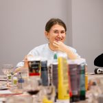 Uśmiechnięta uczestniczka warsztatów siedząca przy stole z farbami i materiałami podczas wydarzenia „Jak malujemy swój wizerunek?” organizowanego przez Twój StartUp.