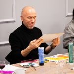 Uczestnik warsztatów trzymający i oglądający własny obraz podczas wydarzenia „Jak malujemy swój wizerunek?” organizowanego przez Twój StartUp