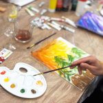 Uczestnicy warsztatów malarskich pracujący nad obrazami, z widoczną paletą farb, pędzlami i materiałami podczas wydarzenia Twój StartUp.